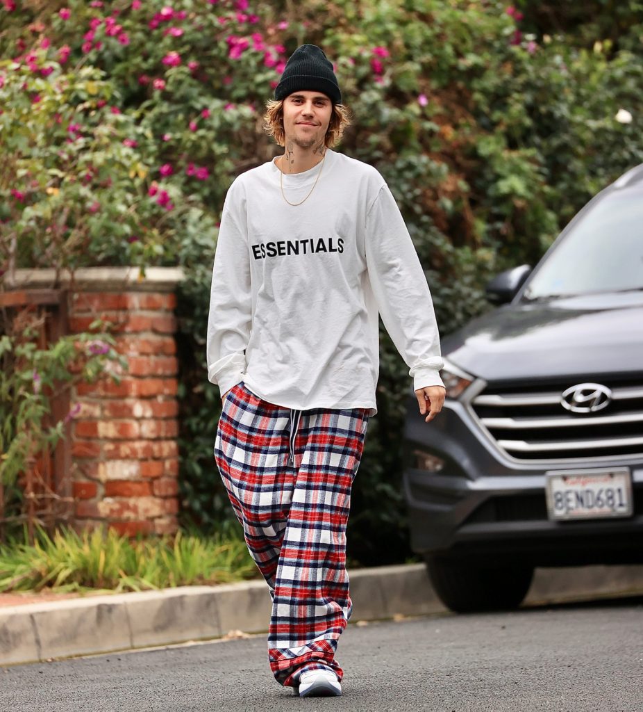 Das Foto zeigt Justin Bieber, wie er auf einer Straße läuft und lächelt. Er trägt eine weite, karierte Hose, einen übergroßen Pullover und eine Mütze.