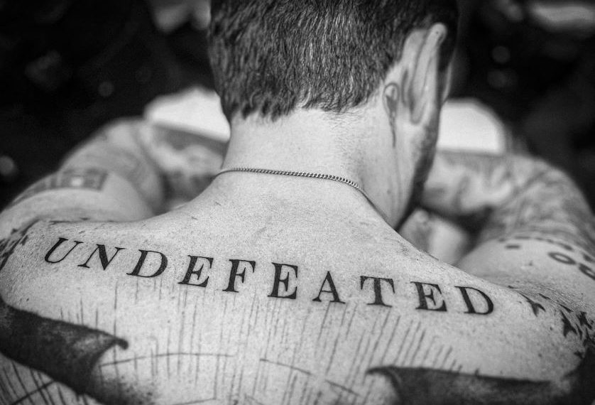 Das Albumcover "Undefeated" von Frank Turner zeigt den Musiker von hinten in schwarz-weiß. Unterhalb seines Nackens ist ein Tattoo mit dem Schriftzug "Undefeated", der zugleich der Albumname ist.