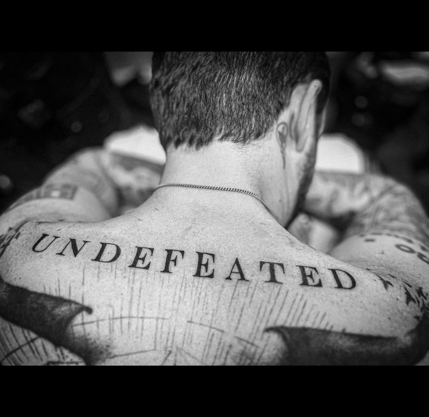 Das Albumcover "Undefeated" von Frank Turner zeigt den Musiker von hinten in schwarz-weiß. Unterhalb seines Nackens ist ein Tattoo mit dem Schriftzug "Undefeated", der zugleich der Albumname ist.